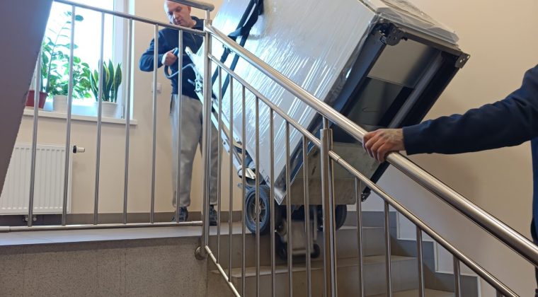 Ekipa transportowa z firmy Manatki24 wnosi lodówkę po schodach w budynku mieszkalnym